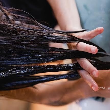Fingers running through hair being washed at a sink.